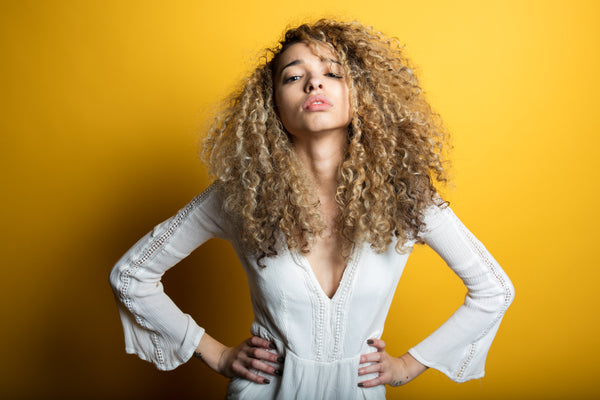 Confident Young Woman Photo A young woman with curly hair poses with her hands on her hips against a bold yellow background.